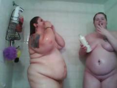 Two huge fat women are in the shower and washing each other